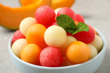 Melon balls and mint in bowl on grey table, closeup