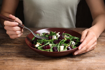 Woman eating fresh delicious beet salad at wooden table, closeup