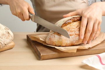 Woman cutting freshly baked bread at wooden table, closeup