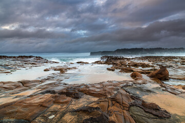 Fototapeta na wymiar Rock platform, cascades and splashes with rain clouds by the seaside