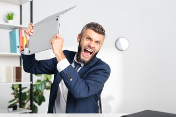 Angry businessman screaming while holding laptop in office