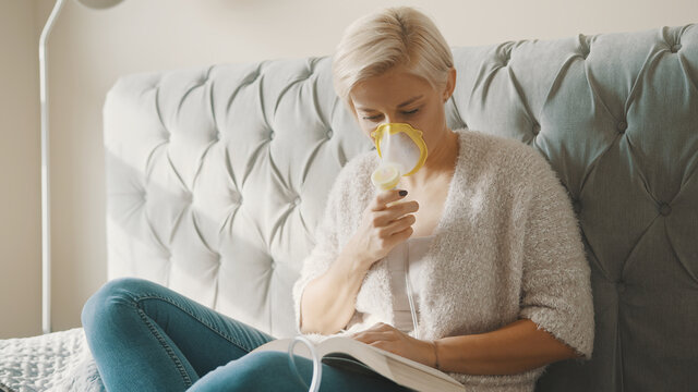 Young blond woman using inhalator or respirator mask in her bedroom. High quality photo