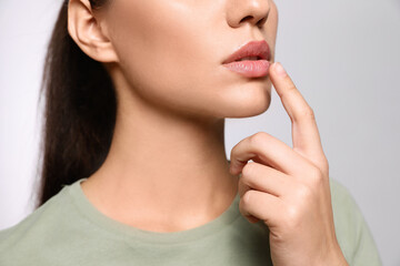 Fototapeta na wymiar Woman with herpes touching lips on light grey background, closeup