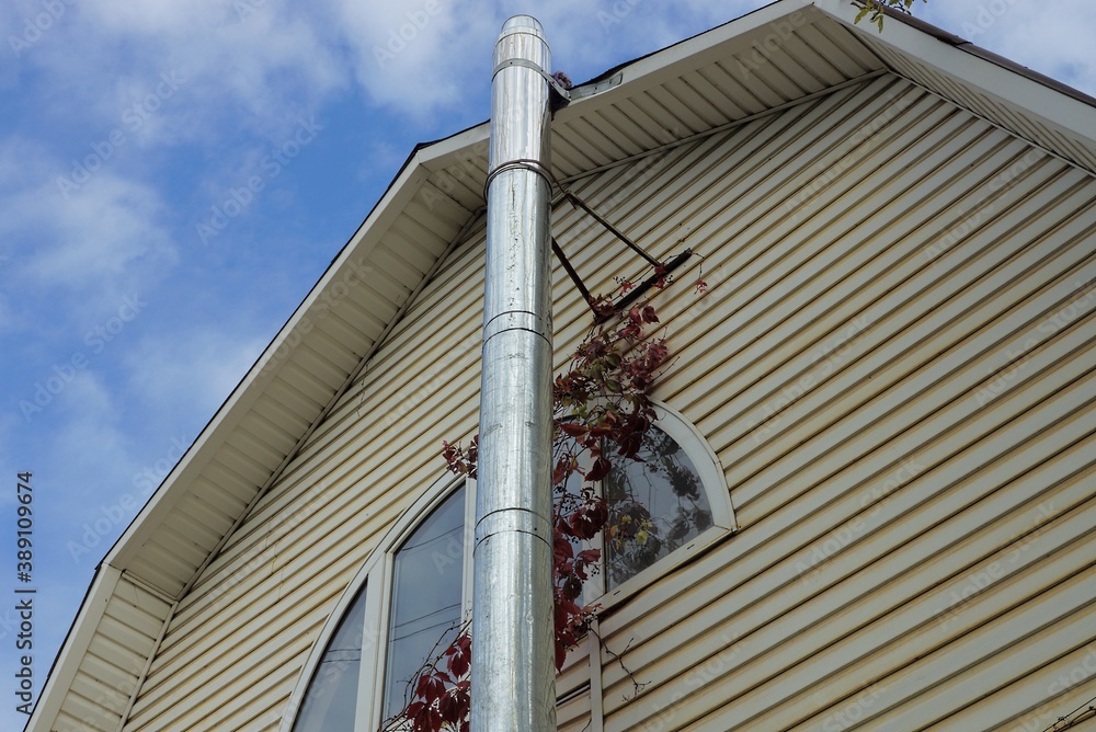 Canvas Prints long gray metal chimney pipe on a brown plastic wall of a house with a window against a blue sky