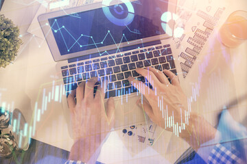 Double exposure of man's hands typing over laptop keyboard and forex chart hologram drawing. Top view. Financial markets concept.