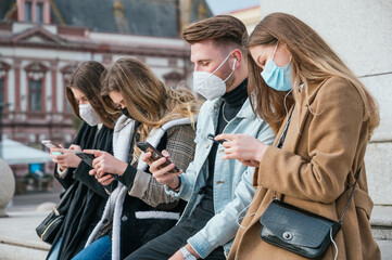Group of young friends wearing face mask and using their smartphones
