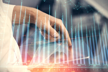 Double exposure of man's hands holding and using a digital device and forex graph drawing. Financial market concept.