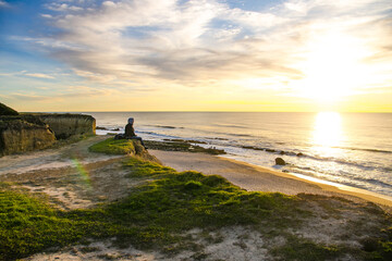 Fototapeta na wymiar A young man sits on the edge of a cliff and enjoys the beautiful view of the beach and sunset.