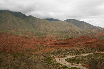 Geology. Panorama view of the red sandstone and rocky mountains, green forest and river flowing across the valley under a cloudy sky in Miranda Slope, La Rioja Argentina. 