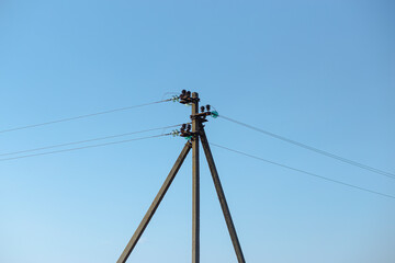 post on the top of which rest high voltage power lines against a blue sky