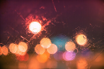 Fototapeta na wymiar Abstract bokeh blur background by rain drops on glass window at night in the city