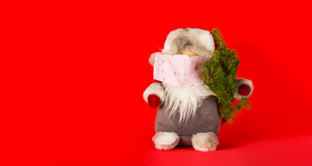 Santa claus in medical mask with christmas tree on red background in minimal style. Christmas holidays in new Covid-19 reality.