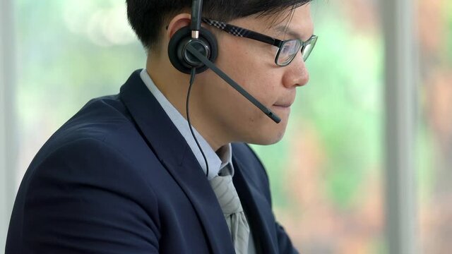 Close up of Confidence Asian businessman customer service call center agent speaking on headset with customer for consulting problem solving. Professional male telesales marketing working in office.