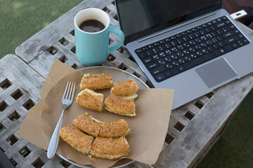 open laptop computer, bread and coffee with outdoor background.