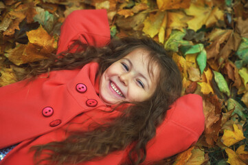 Naklejka na ściany i meble Portrait of a happy little girl lying on autumn leaves in the Park