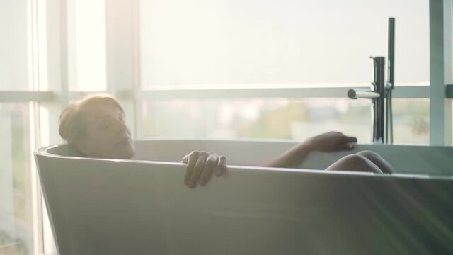 Retired woman taking bath in bathtub against window