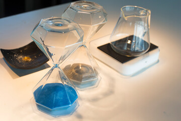 Sand running through the bulbs of an blue hourglass measuring the passing time.