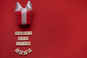 Red gift box with a white ribbon on a red background under the inscription of wooden blocks "happy new year, 2021", with place for text