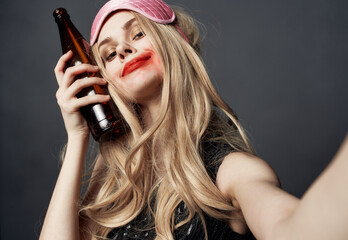 Drunk woman with a bottle of beer on a gray background gestures with her hands and bright makeup