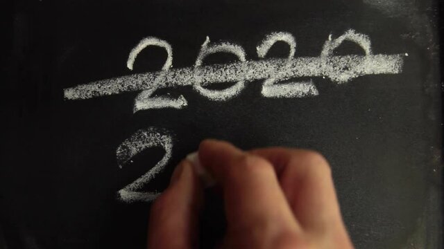 Male hand crosses out the chalk inscription on the school board 2020 and writes the new 2021