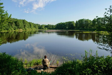 A man is fishing on a forest lake on a Sunny summer morning. Moscow region. Russia.
