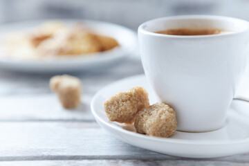 Cup of coffee and brown sugar cubes ( focus on sugar) on bright wooden background. Close up. 