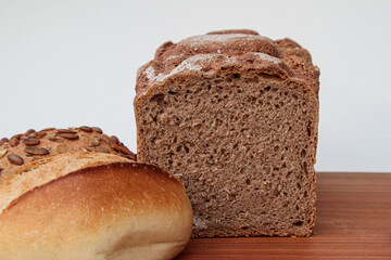 Close-up of an already cut bread and two buns on a wooden table with white background and copy-space