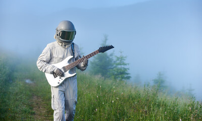 Astronaut in space suit walking on grassy path and playing on guitar. Cosmonaut guitarist with...
