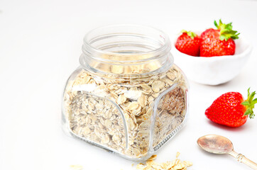 Raw oatmeal in a glass jar, strawberries on a white table