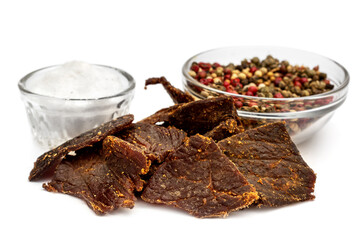 Heap of beef jerky with salt and pepper on white.