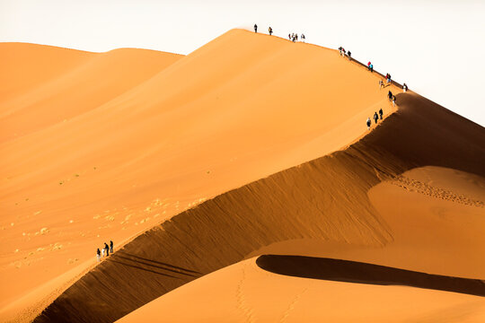 Tourists climbing a large red sand dune in Sossusvlei, Namibia.