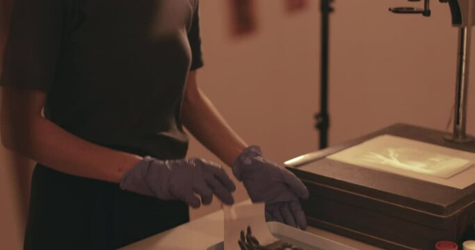 Female photographer developing film and printing photographs in traditional process in darkroom. Portrait of creative girl photographer in photo studio darkroom. Developing analog camera film.