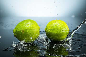 Fototapeta na wymiar Two green limes on gradient background with splash and water drops