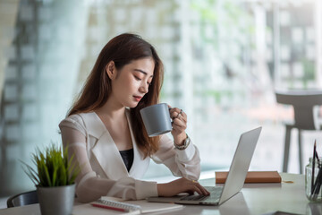 Young asian businesswoman on a coffee break and using laptop computer in office.