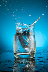 Splash in a glass of water from a falling piece of ice on a blue background