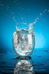 Splash in a glass of water from a falling piece of ice on a blue background