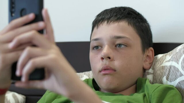 Resting boy lying and playing video games on his  modern phote in an apartment  