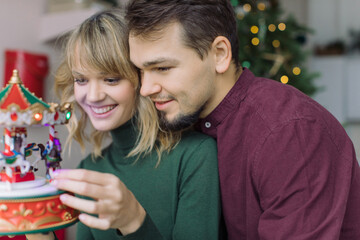 Happy couple in love looking at musical toy Christmas carousel. Christmas holidays at home.