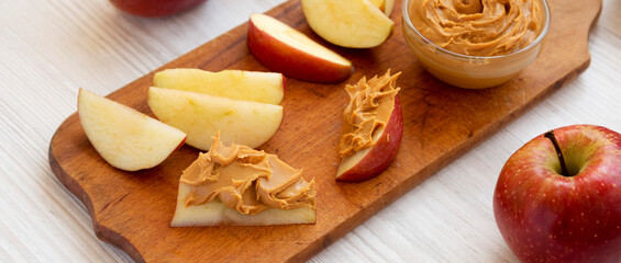 Raw Red Apples and Peanut Butter on a rustic wooden board on a white wooden surface, low angle view.