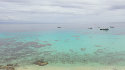 Seascape: Tropical beach with coral reef and turquoise sea with boats. Alorro Beach, Philippines, Samal.