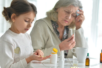 Cute girl giving medicine to sick senior woman