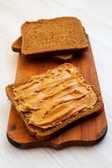 Piece of Bread with Peanut Butter on a white wooden background, side view.