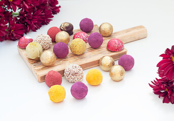 handmade chocolate truffles, different colors on a wooden board on a white background.