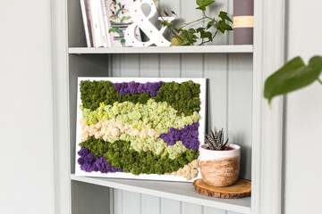 Interior light wall with a picture of moss, white walls, plants, candles and frames ,shelves and books , home and comfort