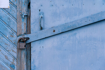 Fragment of an old blue iron-studded door. There is a strong steel locking device and a padlock. Background. Texture.