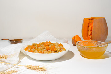 homemade oatmeal porridge with seasonal autumn pumpkin in a white plate on a light background. autumn composition with wheat ears and pumpkin, ingredients for porridge