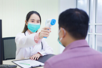 Asian woman doctor uses a infrared forehead thermometer to measure body temperature of patient,...