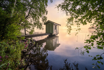 Beautiful morning landscape with little swim cottage, pier and foggy sunrise in lakeside Finland
