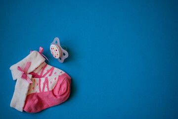 Pink baby socks and pacifier on blue background