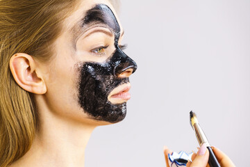 Woman applying black mask to skin face
